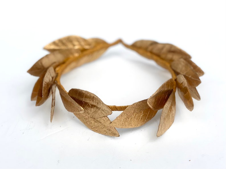 May include: A gold laurel wreath made of metal leaves. The wreath is a circle and is made of many individual leaves.
