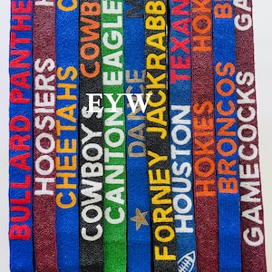 Puede incluir: Una colección de cordones con cuentas de varios colores, cada uno con el nombre de un equipo en letras en negrita. Los cordones tienen cierres dorados y están diseñados para los fanáticos del deporte.