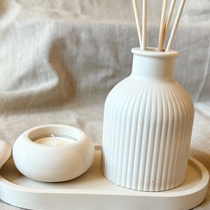 Può includere: Un set di aromaterapia in ceramica bianca con un diffusore a coste con bastoncini di legno, un piccolo portacandele con una candela accesa e un vassoio ovale. Per la profumazione e il relax in casa.