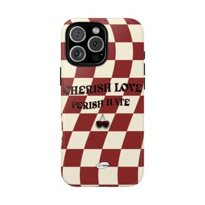 Puede incluir: Funda de teléfono con un patrón de tablero de ajedrez rojo y crema. La funda presenta las palabras "CHERISH LOVE" encima de "PERISH HATE" en negrita. Un par de cerezas debajo.
