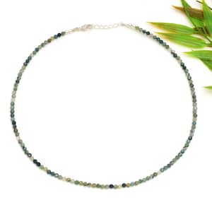 May include: A delicate necklace composed of small, round beads in shades of moss green and white. The necklace has a silver-coloured clasp and chain. The beads are closely strung, creating a subtle, elegant appearance. The necklace is displayed on a white background.