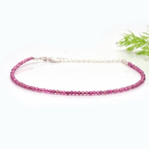 Op de afbeelding: Een delicate armband met kleine, ronde, roze edelstenen aan elkaar geregen. De armband heeft een zilverkleurige sluiting en ketting. De edelstenen hebben een levendige roze tint, wat een elegant sieraad creëert.