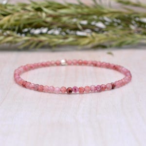 Peut inclure: Un bracelet délicat composé de perles roses. Le bracelet est fait de petites perles rondes et facettées de différentes nuances de rose, avec quelques perles rouge-rose plus foncées parsemées. Le bracelet est enfilé sur un cordon fin et élastique.