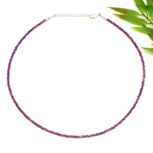 May include: A delicate necklace featuring small, faceted, magenta-colored beads. The necklace has a silver-colored chain and clasp. The beads are strung closely together, forming a continuous strand. The necklace is displayed against a white background.