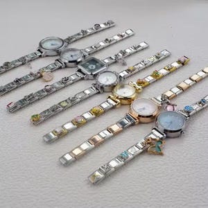 Könnte beinhalten: Eine Sammlung von Charm-Uhren mit verschiedenen Zifferblattformen und -farben. Die Armbänder sind silberfarben mit dekorativen Charms. Einige Uhren haben gold- oder roségoldfarbene Akzente. Die Zifferblätter sind weiß, blau und silber.