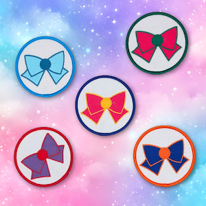 May include: Five embroidered patches featuring colorful bow designs. Each patch has a white background with a colored bow in the center, surrounded by a colored border. The bows are in shades of blue, pink, purple, and orange.