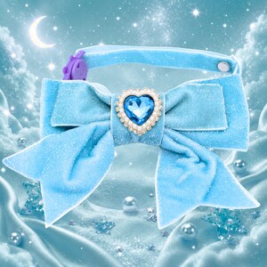 May include: A light blue pet collar with a large bow. The bow features a heart-shaped jewel with a blue center and a pearl-like border. The collar has a purple clasp and a matching blue strap. The background is a dreamy, celestial scene.