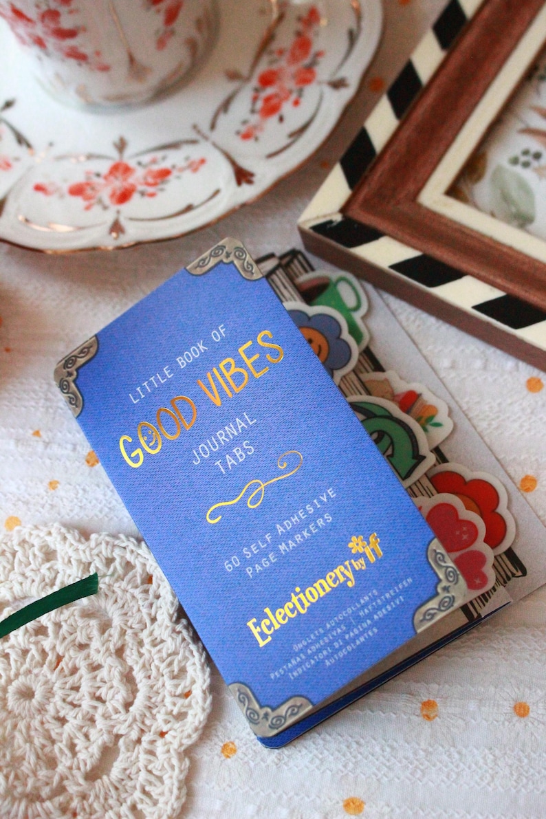 Pode incluir: Um di&aacute;rio azul com letras douradas "Little Book of Good Vibes" e cantos decorativos. Cont&eacute;m 60 marcadores de p&aacute;gina autocolantes. Autocolantes florais e smiley coloridos tamb&eacute;m s&atilde;o vis&iacute;veis.