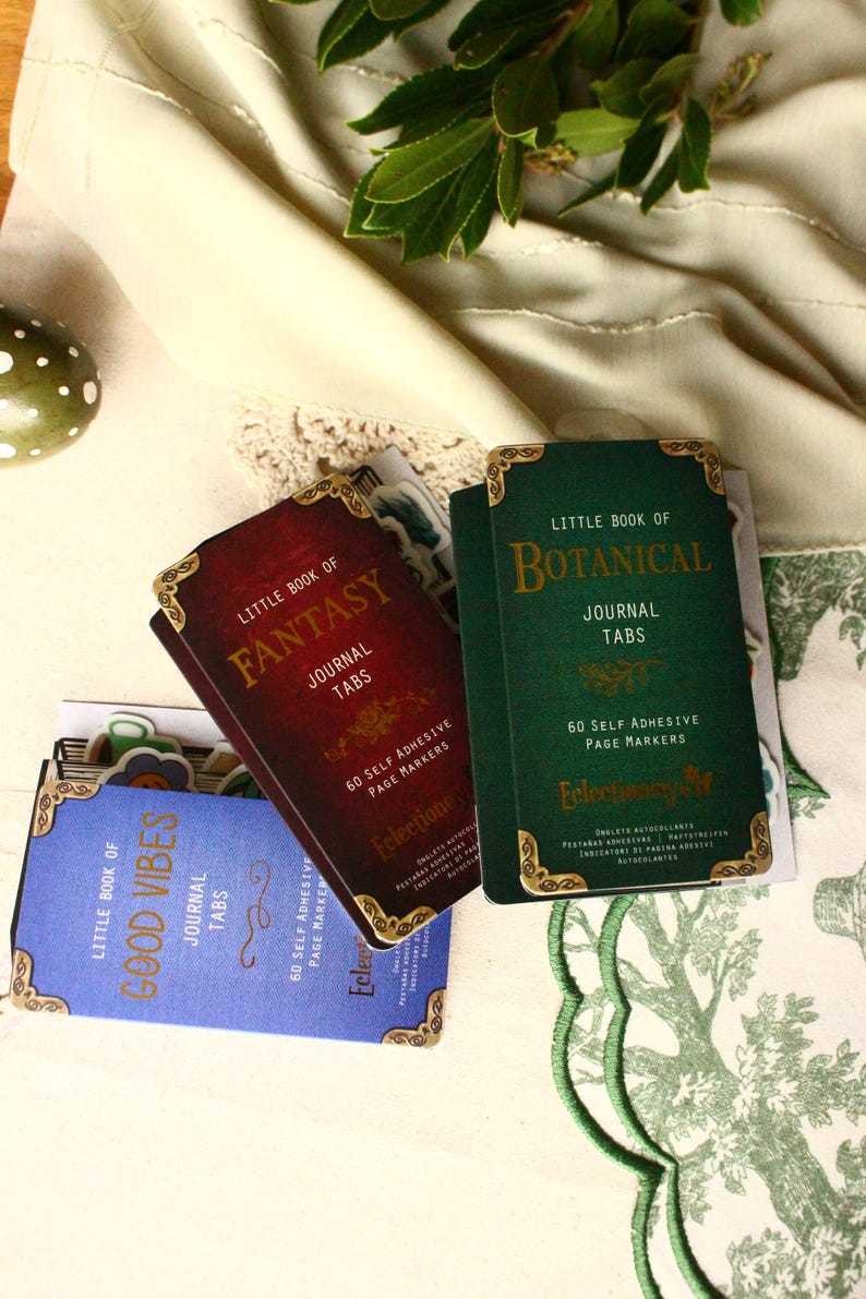 Pode incluir: Um conjunto de abas de di&aacute;rio com bordas douradas decorativas. As abas s&atilde;o rotuladas como "Little Book of Fantasy", "Little Book of Botanical" e "Little Book of Good Vibes". Cada conjunto cont&eacute;m 60 marcadores de p&aacute;gina autoadesivos.