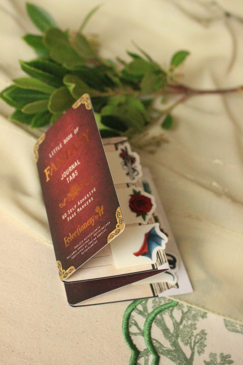 Pode incluir: Um conjunto de abas de di&aacute;rio "Little Book of Fantasy" em bord&ocirc; com detalhes dourados. O conjunto inclui 60 marcadores de p&aacute;gina autocolantes. As abas decorativas apresentam rosas e um design de asa de morcego.