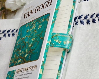 Peut inclure: Un carnet blanc avec une couverture turquoise représentant une peinture de Van Gogh et le texte "VAN GOGH" et "MEET VAN GOGH". Le carnet est ouvert, révélant des pages lignées et une sangle de fermeture turquoise.