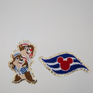 May include: Embroidered patches featuring Chip and Dale in sailor outfits and a blue and white flag with a red Mickey Mouse head. The patches have gold glitter borders on a white background.
