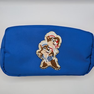 May include: A royal blue cosmetic bag with a Chip and Dale embroidered patch. The patch features the cartoon characters in sailor outfits with gold trim. The bag is rectangular with a zipper closure.
