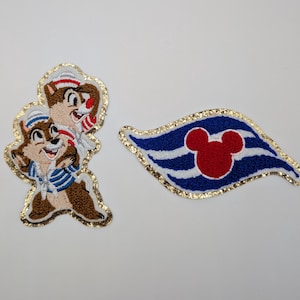 May include: Embroidered patches featuring Chip and Dale in sailor outfits and a Mickey Mouse-themed flag. The Chip and Dale patch has a gold glitter border. The flag patch is blue, white, and red with a gold glitter border.