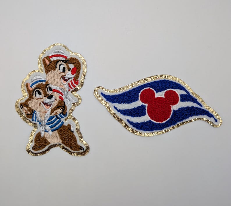 May include: Embroidered patches featuring Chip and Dale in sailor outfits and a Mickey Mouse-themed flag. The Chip and Dale patch has a gold glitter border. The flag patch is blue, white, and red with a gold glitter border.