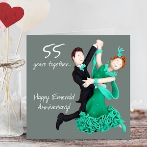 May include: A greeting card with a grey background features a dancing couple figurine. The man wears a black tuxedo and the woman a green dress. Text reads "55 years together..." and "Happy Emerald Anniversary!"