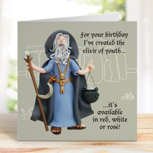 May include: Greeting card with a wizard figurine in blue robes and a black cloak. The card has text that reads "for your birthday I've created the elixir of youth... it's available in red, white or rosé!"