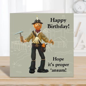 May include: A birthday card with a clay model of a miner, holding a pickaxe. The figure is dressed in a brown hat, jacket, and black boots. The card reads "Happy Birthday!" and "Hope it's proper 'ansum!" on a light grey background.