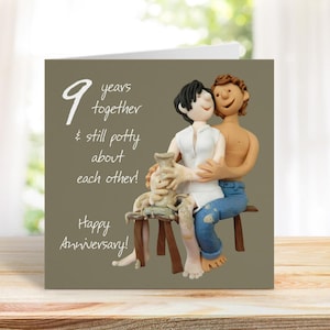 May include: A greetings card featuring a clay sculpture of a couple. The card reads "9 years together & still potty about each other! Happy Anniversary!" The couple is seated on a wooden bench. The woman wears a white shirt, the man is shirtless.