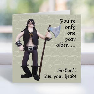 May include: Birthday card with a clay figure of a character in a black vest and boots, holding an axe. The card has the text "You're only one year older... So don't lose your head!" on a light green background.