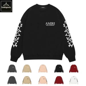 Pode incluir: Camisola preta de gola redonda com design de ossos brancos nas mangas. A camisola tem a palavra "AMIRI" e "HOLLYWOOD.CA" impressas em branco no peito. Várias outras opções de cores são exibidas abaixo.