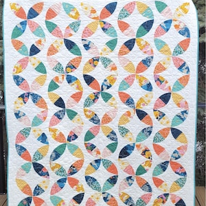 May include: A vibrant quilt featuring a repeating design of petal-like shapes in orange, pink, blue, yellow, and green. The quilt is set against a white backdrop with a light blue border. The text "Tangerine Quilt" and "Baby, Throw, and Bed" are visible.