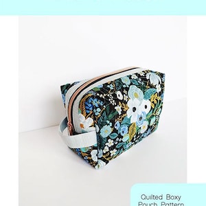 May include: A quilted boxy pouch with a floral pattern in white, blue, and yellow on a black background. The pouch has a zip closure and a striped handle. The text "Holland Pouch" is at the top.