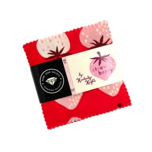 May include: A stack of red fabric squares with a strawberry pattern. A label reads "Strawberry" and "by Kimberly Kight." The stack is held together with a black band that reads "Ruby Star Society" and "Guaranteed Delightful."
