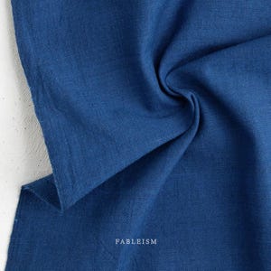 May include: A close-up of a folded piece of indigo blue fabric. The fabric is textured and appears to be linen or a similar material. The word "FABLEISM" is printed in white at the bottom right corner of the image.