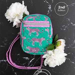 Pode incluir: Uma bolsa transversal verde-azulado com um design de estampa de leopardo rosa e uma alça rosa. A bolsa tem fecho de zíper e é cercada por flores brancas. O texto "Athena Crossbody" está no topo.