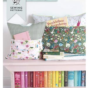 May include: A reading pillow pattern with a variety of fabric patterns, including floral, striped, and a village scene. The pillow has pockets for books and a pen. The image also shows a shelf with colorful books and the text "READING PILLOW PATTERN".