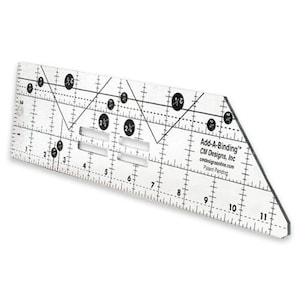May include: A clear acrylic quilting ruler labeled Add-A-Binding by CM Designs, Inc. The tool features black printed markings, including an 11-inch scale, various angle lines, and circular measurement indicators. It has four rectangular slots.