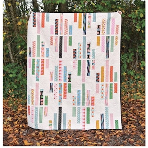 May include: The Vivian Quilt pattern by Erica Jackman. A white quilt with colourful vertical stripes in various patterns and colours, including pink, orange, green, and blue. The quilt is displayed outdoors, with text at the bottom indicating sizes and quilting information.