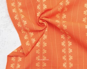 May include: A vibrant orange fabric featuring a repeating vertical pattern of light yellow floral motifs and thin, delicate stripes. The textile displays a soft, folded texture with the word FABLEISM printed in small, clear white letters.