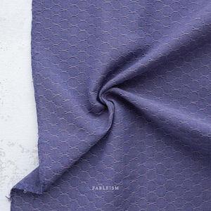 May include: Close-up of a textured, indigo-colored fabric with a repeating geometric pattern. The fabric is draped, showing folds and shadows. The word "FABLEISM" is printed on the fabric.