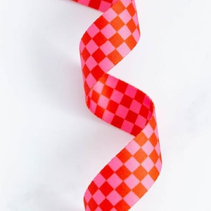 May include: A vibrant ribbon with a checkerboard pattern in shades of red and pink. The ribbon is curled, creating a dynamic visual against a white background. This decorative ribbon is suitable for crafts and gift wrapping.