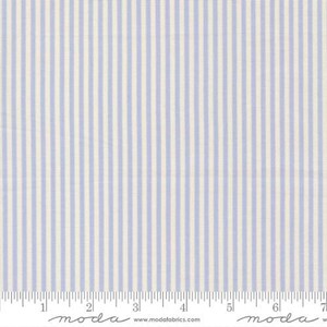 May include: Close-up of fabric with vertical stripes in light blue and off-white. The fabric has a ruler along the bottom edge, with the word "moda" printed on it. The fabric is likely used for quilting or sewing projects.