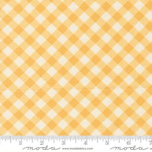 May include: A close-up of a fabric with a yellow and cream-colored gingham pattern. The pattern is a classic checkered design, with the squares arranged diagonally. A ruler is at the bottom of the image, with the word "moda" and a website address printed on it.