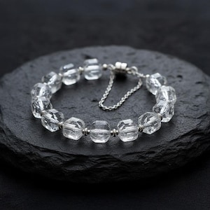 Könnte beinhalten: Ein Armband aus klarem Quarz-Kristall mit facettierten Perlen. Das Armband hat eine silberfarbene Kette und einen Verschluss. Die Perlen sind mit silberfarbenem Metall aufgefädelt. Das Armband wird auf einer schwarzen Oberfläche präsentiert.