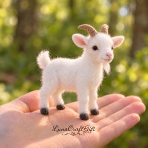 May include: A small, white, needle-felted goat figurine with light brown horns and dark gray hooves. The goat has a textured, woolly appearance, pointed ears, and a small beard. The text LunaCraftGifts is printed in black script on the surface.