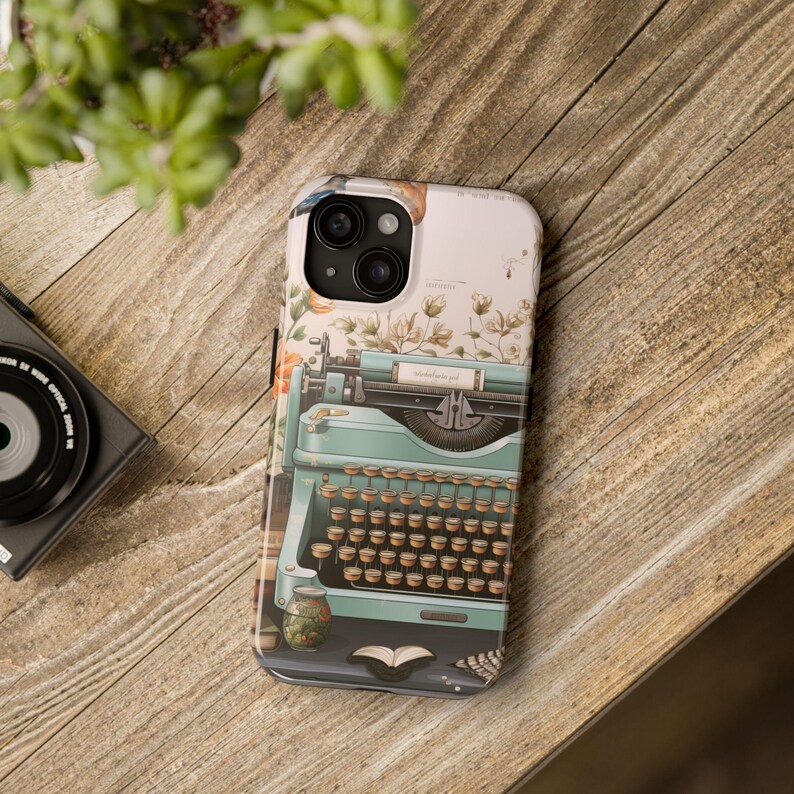 May include: A phone case with a vintage typewriter design. The typewriter is blue and green with a floral background. The case has a cutout for the phone's camera.