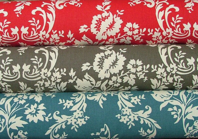 Op de afbeelding: Drie stofstalen met een wit bloemenpatroon op verschillende gekleurde achtergronden. De bovenste staal is rood, de middelste staal is grijs en de onderste staal is teal.