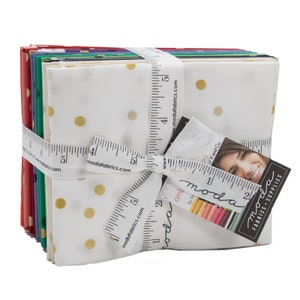 May include: A stack of 12 fat quarters of fabric featuring a white background with gold polka dots. The fabric is tied with a white ribbon and a measuring tape that reads "modafabrics.com". The fabric is labelled "ombre by va of V and Co."