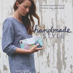 May include: A book cover featuring a woman holding a colorful fabric pouch. The title of the book is "handmade style" and the subtitle is "23 must-have basics to stitch, use, and wear". The book is by Anna Graham, creator of noodlehead.