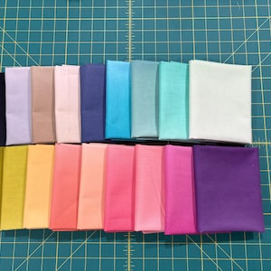 May include: A collection of 20 fabric swatches in various colors, including purple, green, blue, pink, and yellow. The swatches are arranged in a rainbow pattern.