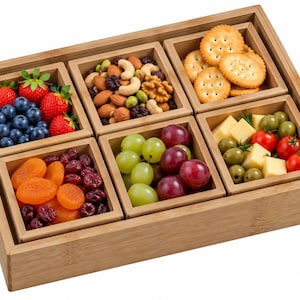 May include: A rectangular bamboo serving tray containing six square bamboo bowls. The bowls are filled with various food items including strawberries, blueberries, mixed nuts, round crackers, dried apricots, cranberries, green and red grapes, cheese cubes, olives, and cherry tomatoes.