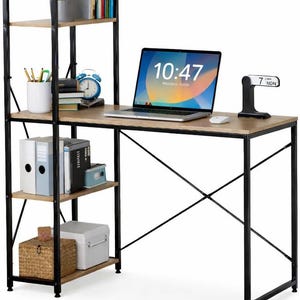 May include: A desk with attached shelving, featuring a light brown wooden surface and black metal frame. A laptop displays 10:47 on the screen. The desk includes a small clock and calendar. Shelves hold books and office supplies.