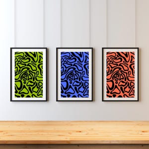 Könnte beinhalten: Drei gerahmte abstrakte Kunstdrucke. Jeder Druck weist ein einzigartiges Farbschema auf: Grün mit Schwarz, Blau mit Schwarz und Koralle mit Schwarz. Die abstrakten Designs bestehen aus organischen, fließenden Formen. Die Rahmen sind schwarz, und die Drucke werden an einer weißen Wand gezeigt.