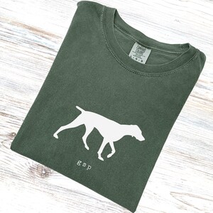 Puede incluir: Camiseta verde oscuro con una silueta blanca de perro y las letras "gsp" impresas debajo. La camiseta está doblada y tiene una etiqueta Comfort Colors.
