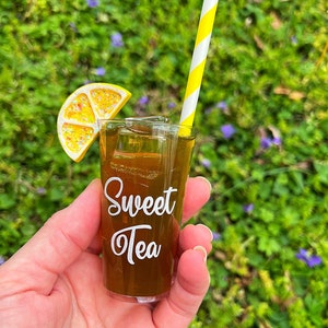 May include: A miniature glass of iced tea with a lemon wedge and a yellow and white striped straw. The glass has the words "Sweet Tea" printed on it.